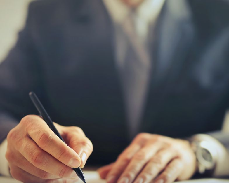 Person in a suit writing on paper with a pen at a desk