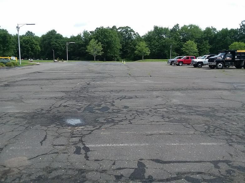 Empty cracked parking lot with a few parked cars and trees in the background