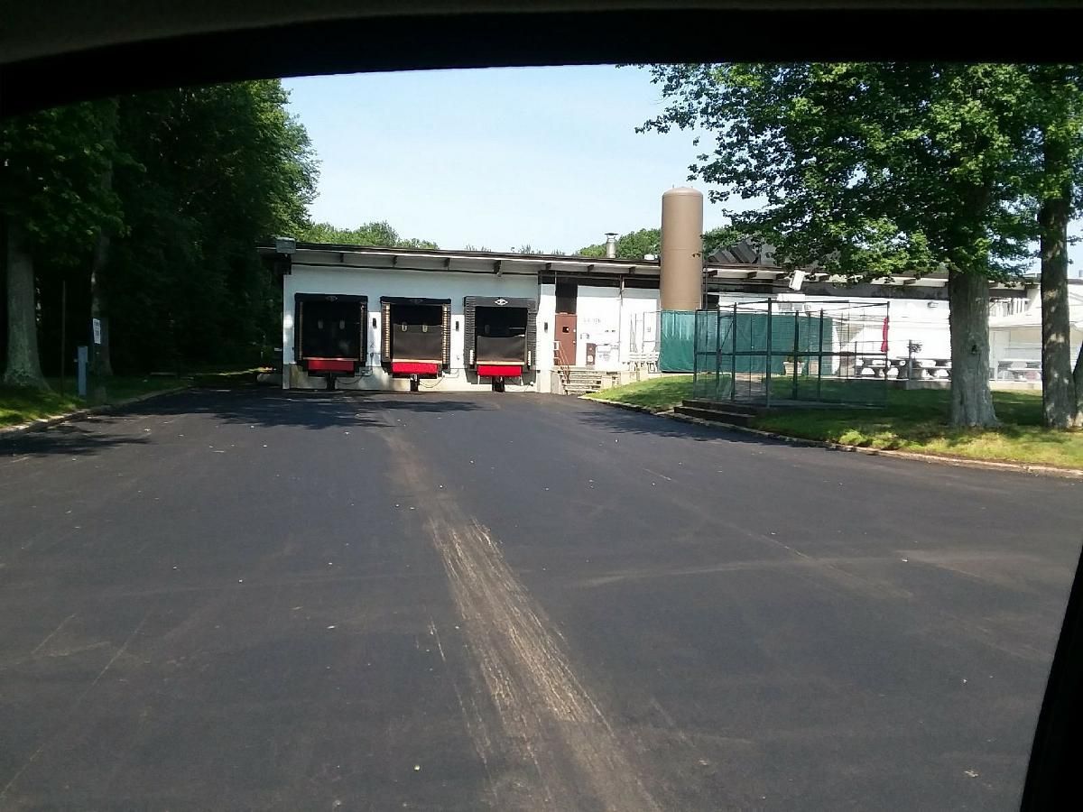 Three red fire trucks parked in a garage at the end of a paved road, with trees and a fence nearby
