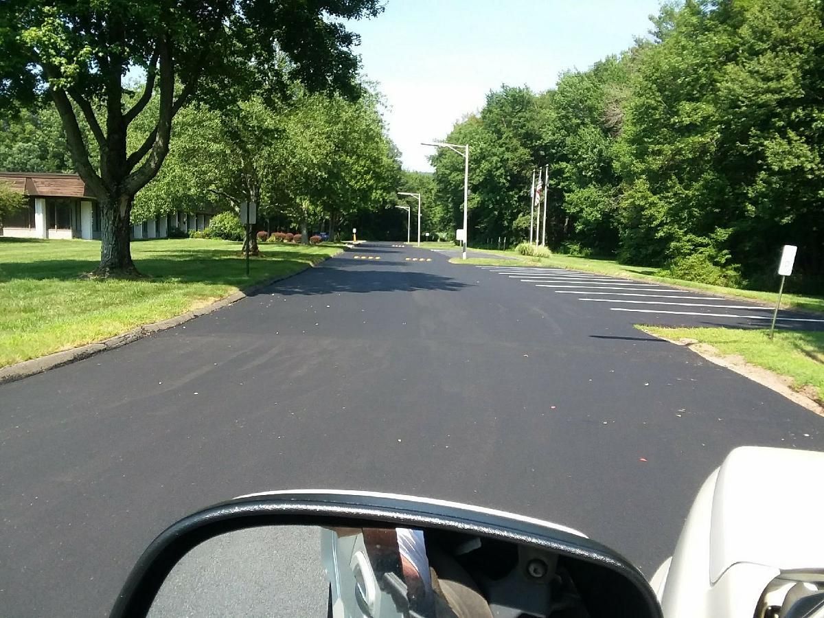 Quiet tree-lined suburban street with a freshly paved black road and green lawns on both sides