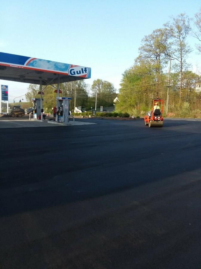 Gas station forecourt with a Gulf canopy and a small orange vehicle on a wide blacktop, trees in background