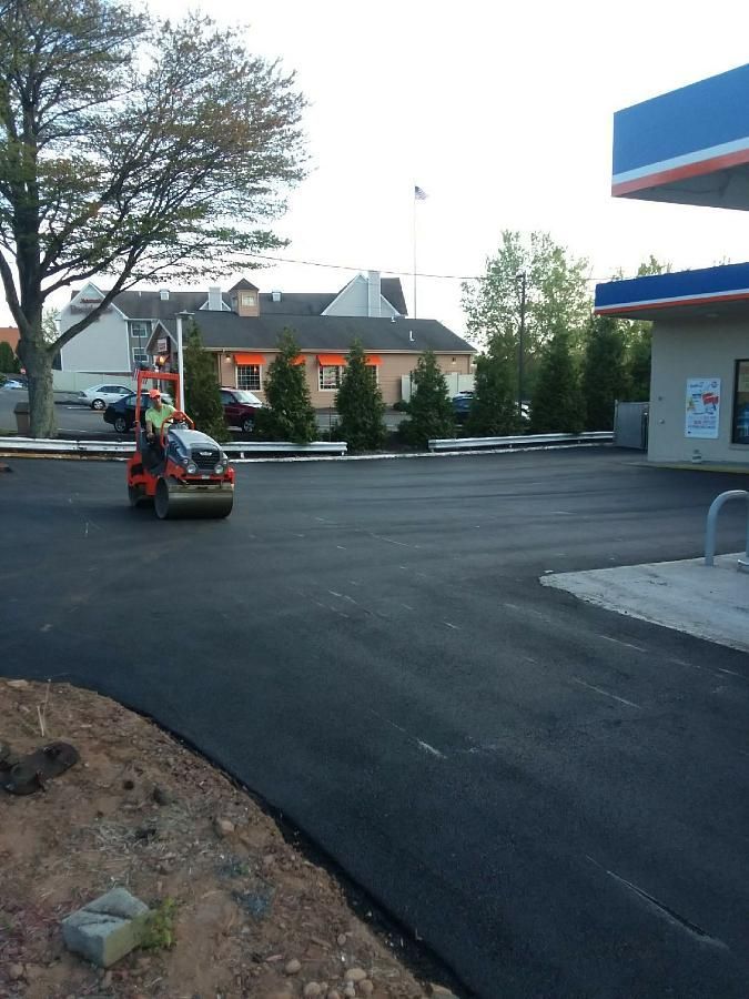 Small utility vehicle on a paved lot near a gas station, with trees and buildings in the background.