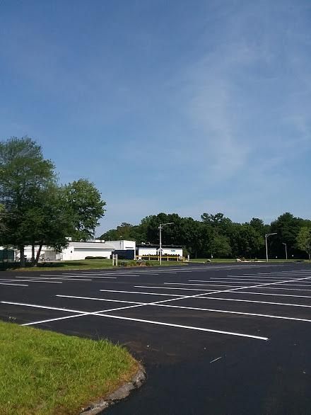 Empty parking lot with white lines, a small building, trees, and blue sky