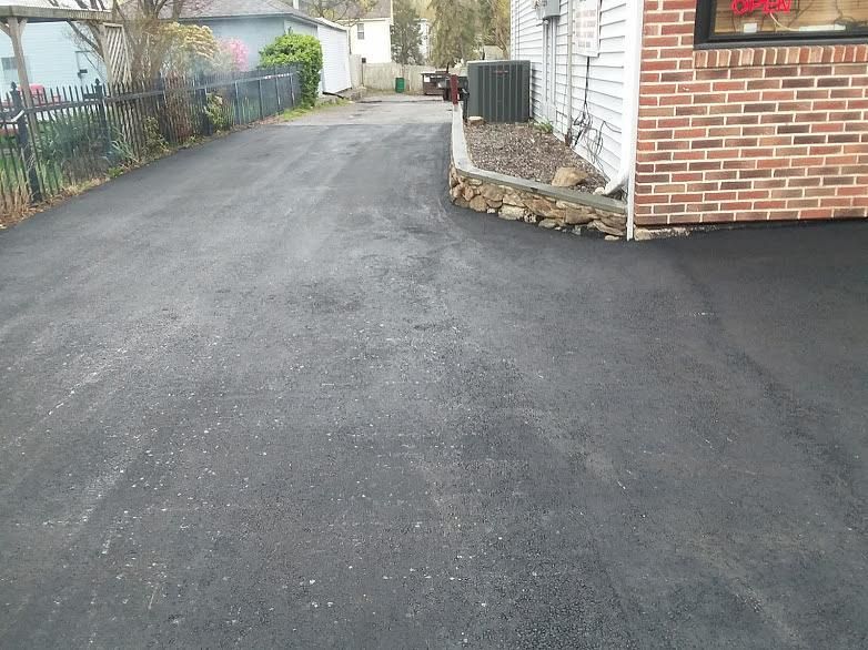 Residential driveway with fresh black asphalt beside a brick house and stone landscaping border