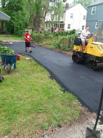 Fresh black asphalt being laid on a driveway, with workers and a child nearby in a residential yard.