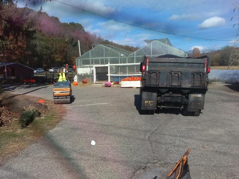 Construction site with dump truck, roller, and greenhouse under a blue sky