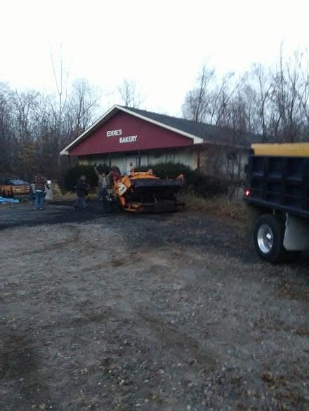 Dump truck and orange tractor parked outside a red building with a white sign, in a gravel lot at dusk