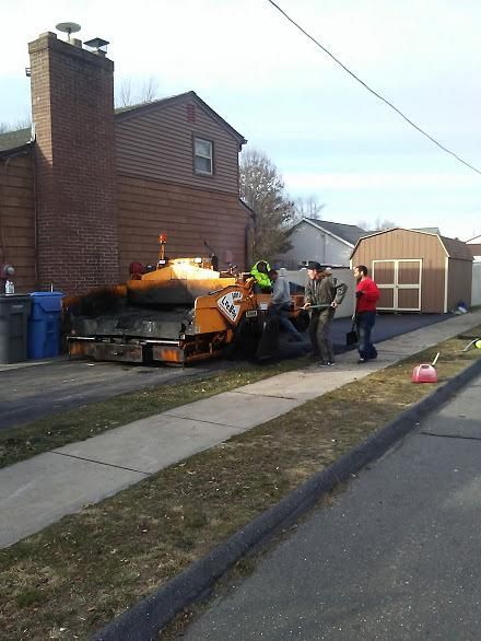Workers loading a large wrapped item onto a trailer beside a brick house on a suburban street