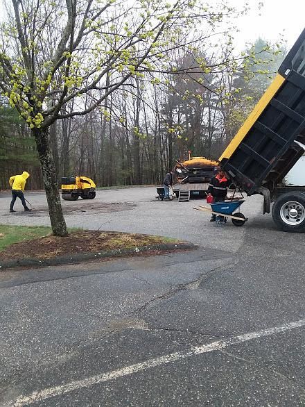 Workers operating a yellow dump truck on a wet road in a wooded area