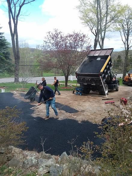 Workers paving a driveway with fresh black asphalt beside a dump truck outdoors