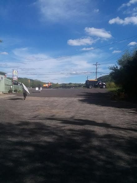 Quiet rural roadside under a blue sky, with a person walking and cars near small buildings.