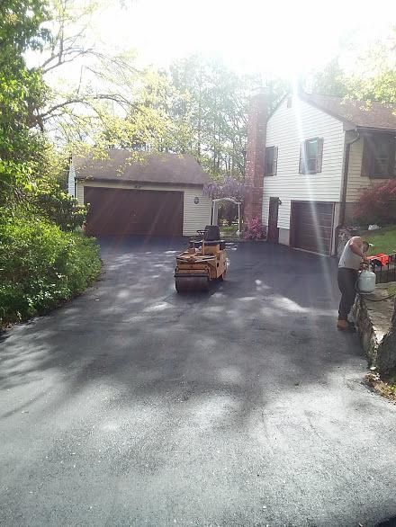 Driveway with a garage, two parked vehicles, and a person watering plants beside a house.