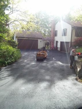 Curved driveway leading to a large house with manicured landscaping under a bright blue, cloudy sky