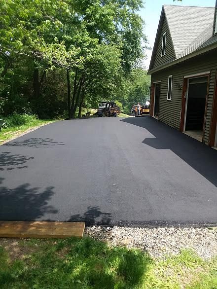Freshly paved black asphalt driveway beside a house and trees on a sunny day