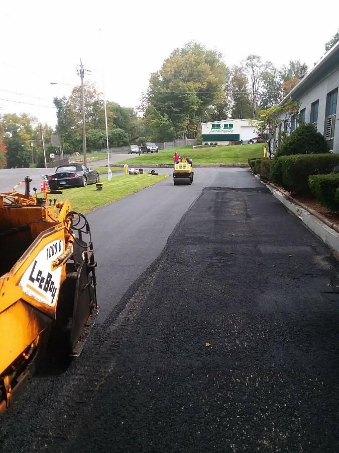 Road paving work on a residential street with an orange roller and black fresh asphalt.