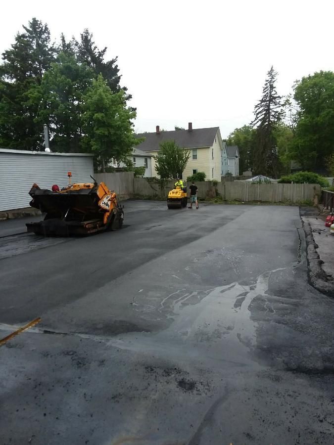 Freshly paved parking lot with two road rollers near a white wall and trees
