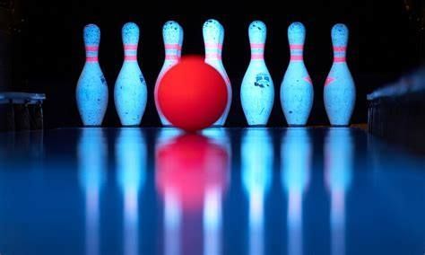 Red bowling ball rolling towards bowling pins. Pins glow blue under blacklight.