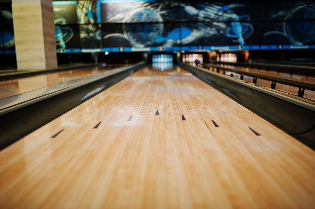 Bowling lane, perspective view. Wood lane with black gutters leads to pins at the far end, bowling alley setting.