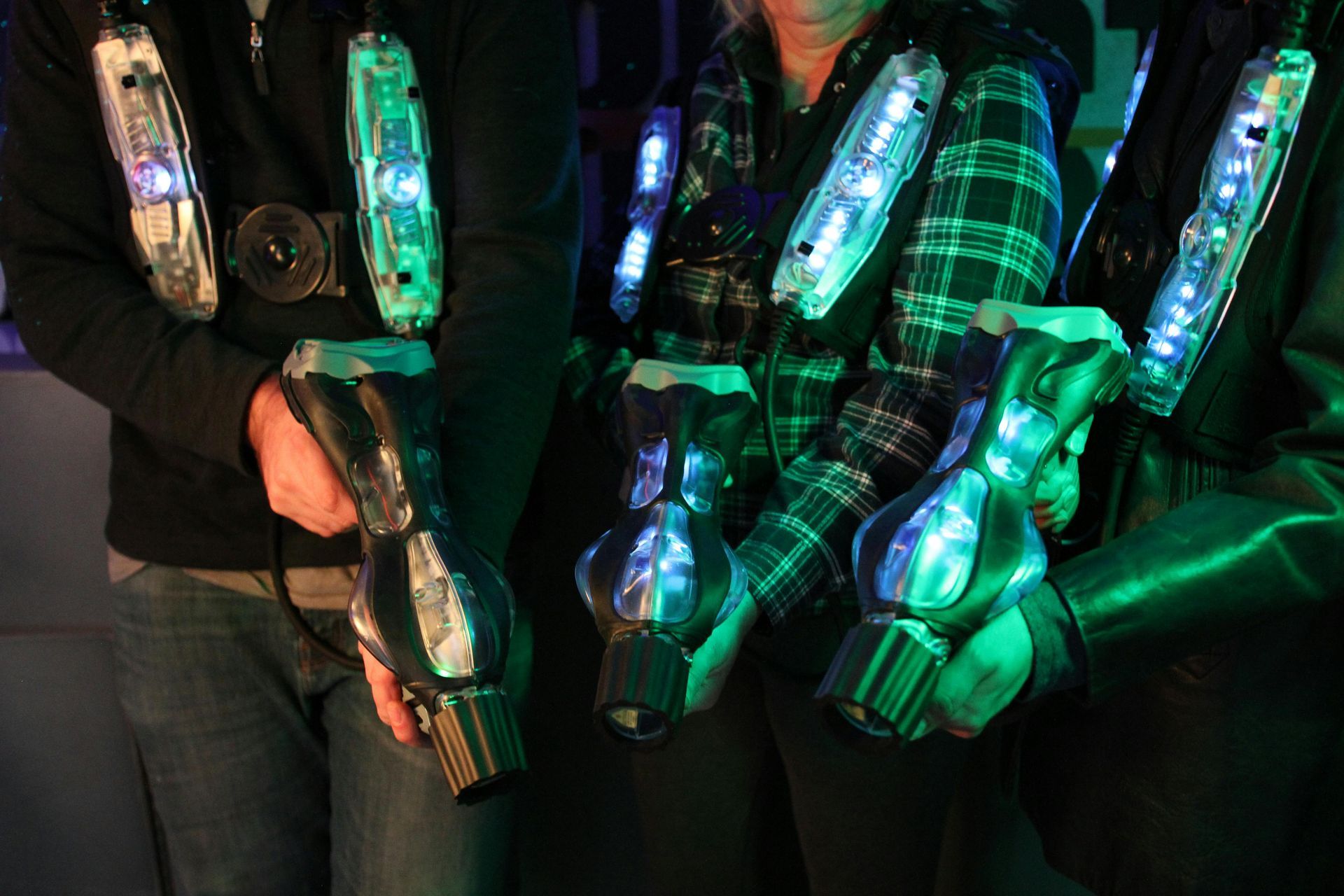 People in a dimly lit setting, holding laser tag guns, with glowing chest packs.