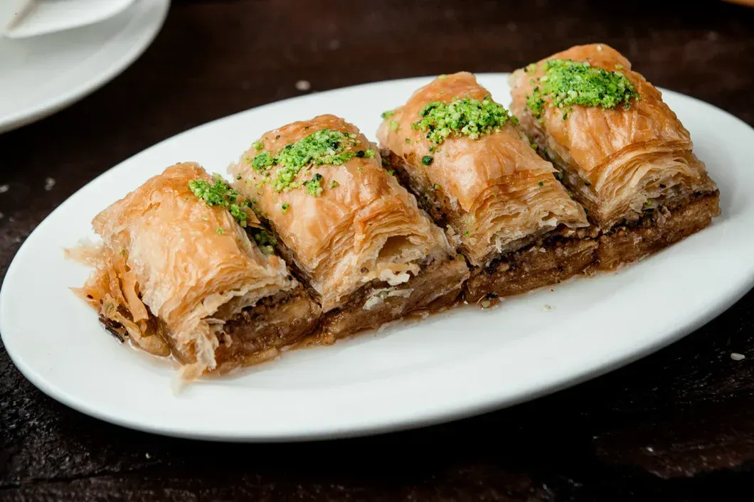 A white plate topped with baklava and pistachios on a table.