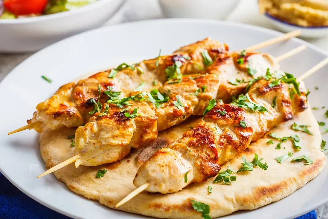 Chicken skewers on naan bread on a white plate.