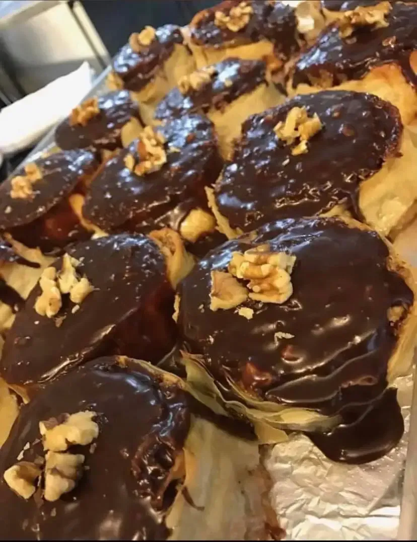 A bunch of chocolate covered pastries with walnuts on top