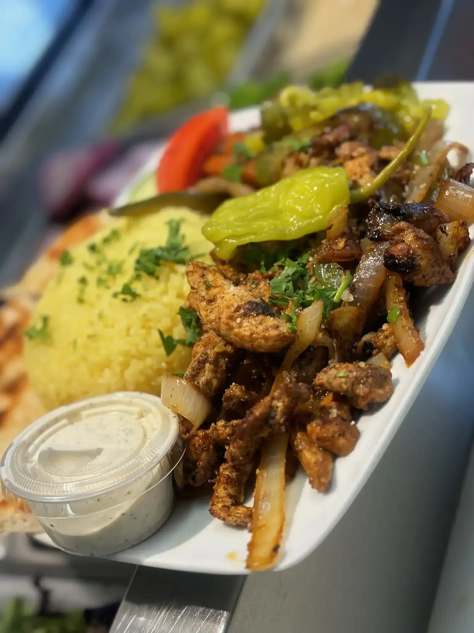 A white plate topped with meat , rice , vegetables and a dipping sauce.