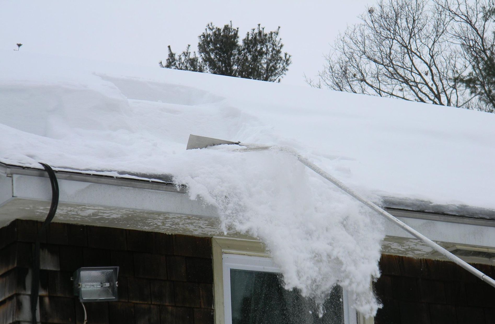 A Man Is Using A Snow Blower To Clear Snow From The Sidewalk — Brimfield, MA — RMD Services, Inc. A Man Is Using A Snow Blower To Clear Snow From The Sidewalk — Brimfield, MA — RMD Services, Inc.