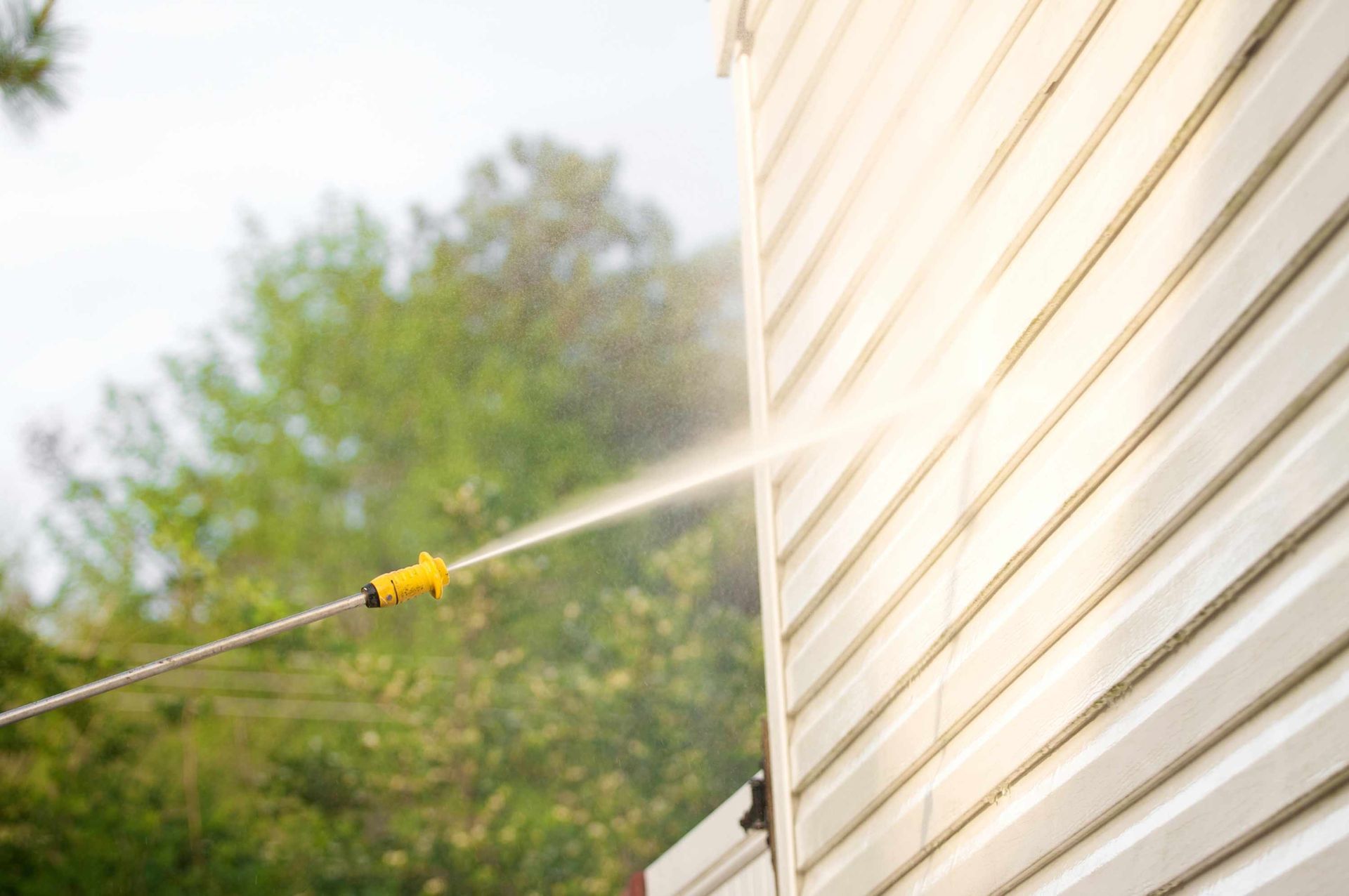 A Person Is Using A High Pressure Washer To Clean The Side Of A House — Brimfield, MA — RMD Services, Inc. A Person Is Using A High Pressure Washer To Clean The Side Of A House — Brimfield, MA — RMD Services, Inc.