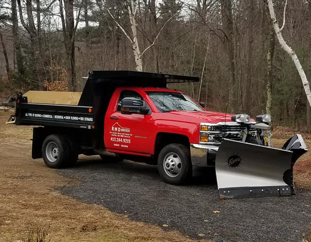 A Small House With A Satellite Dish On The Roof Is Sitting In The Middle Of A Forest — Brimfield, MA — RMD Services, Inc. A red dump truck with a snow plow attached to it.