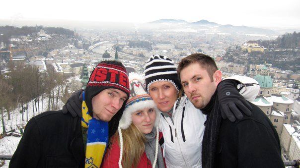 Four people in winter hats pose with a snowy cityscape background.