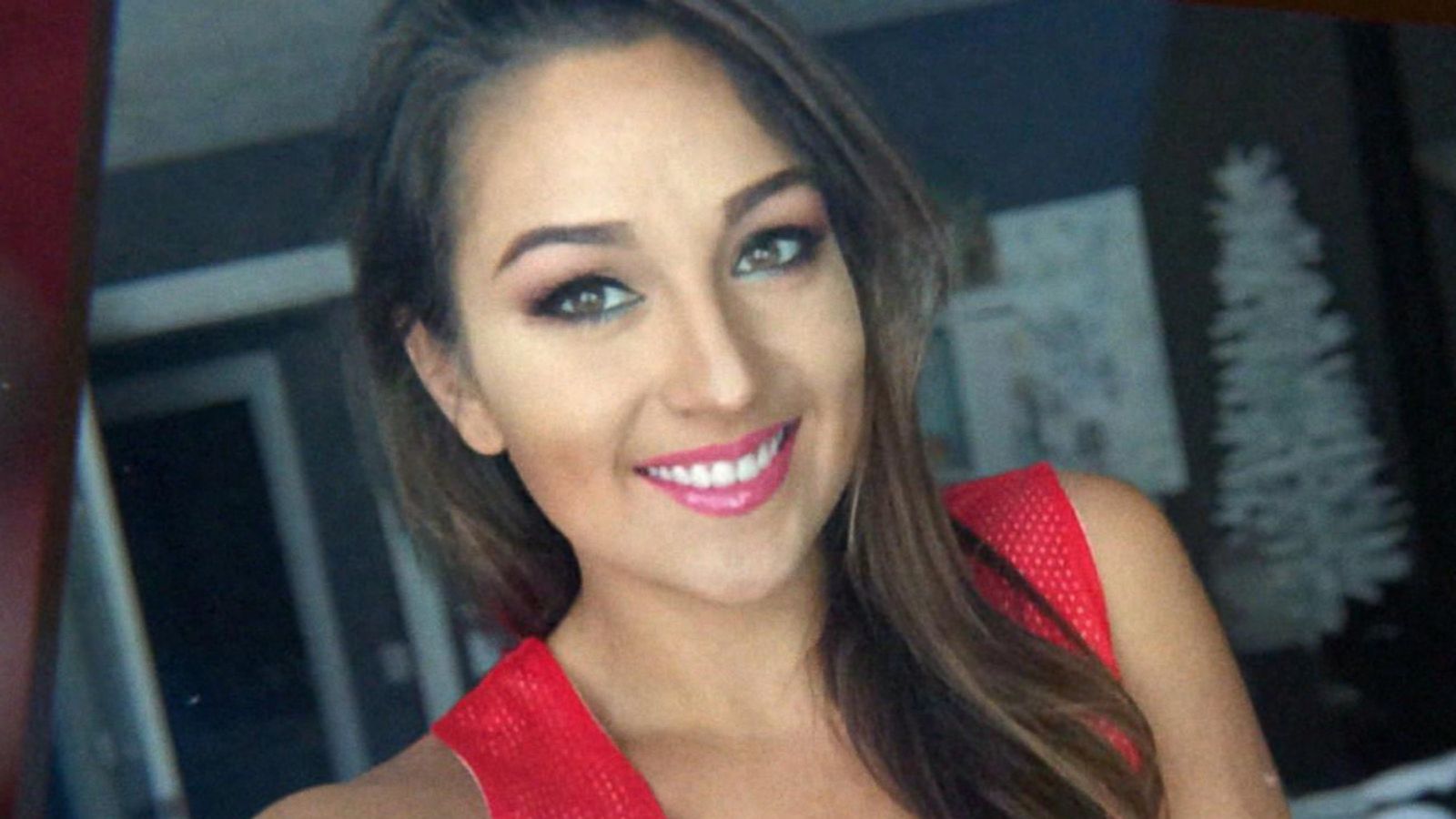 Woman with long brown hair, wearing a red top, smiles at the camera.