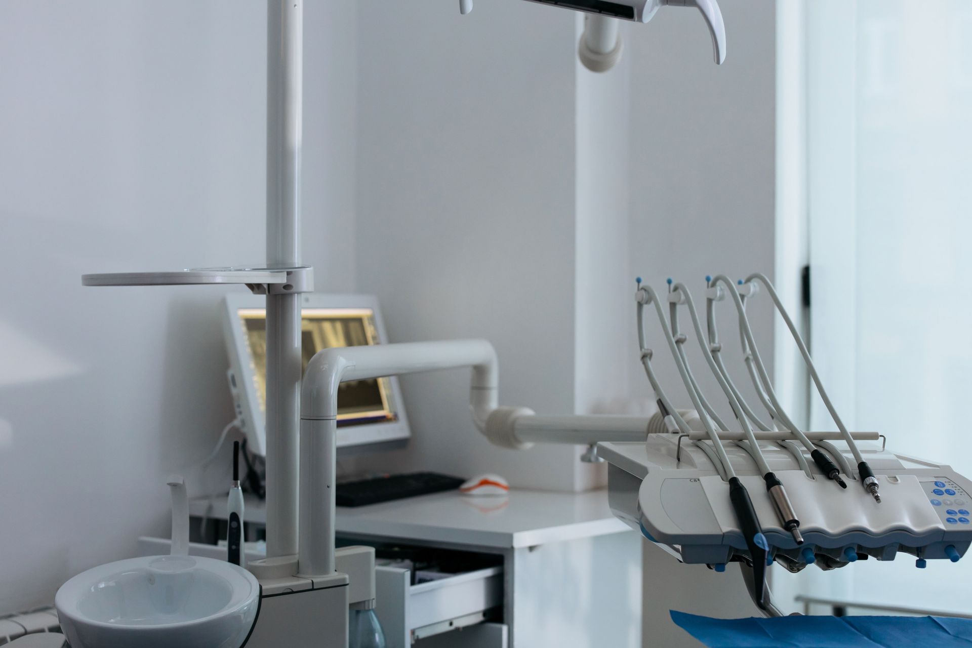 Dental clinic room with treatment chair, overhead light, and dental tools by a bright window