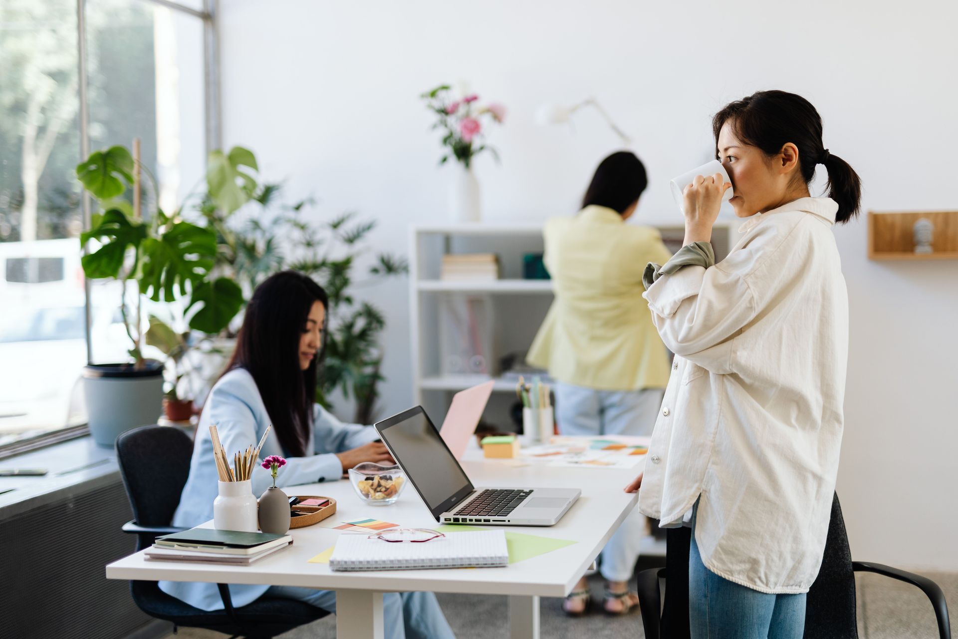 People working in a bright office, with one person taking a photo beside a desk.