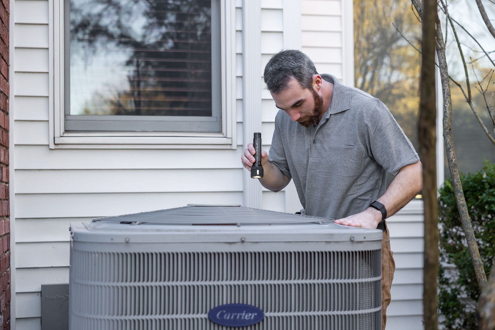 Technician inspecting an outdoor air conditioner unit beside a house window