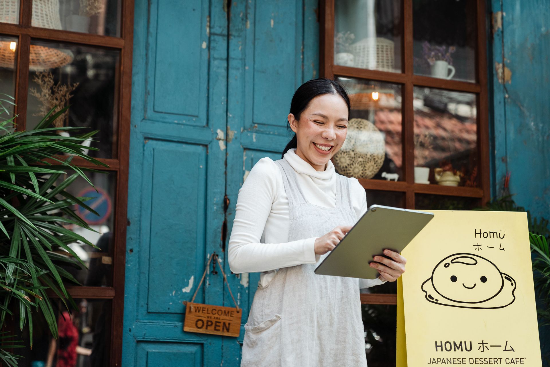 Woman smiling outside a blue storefront, holding a clipboard beside a shop sign.