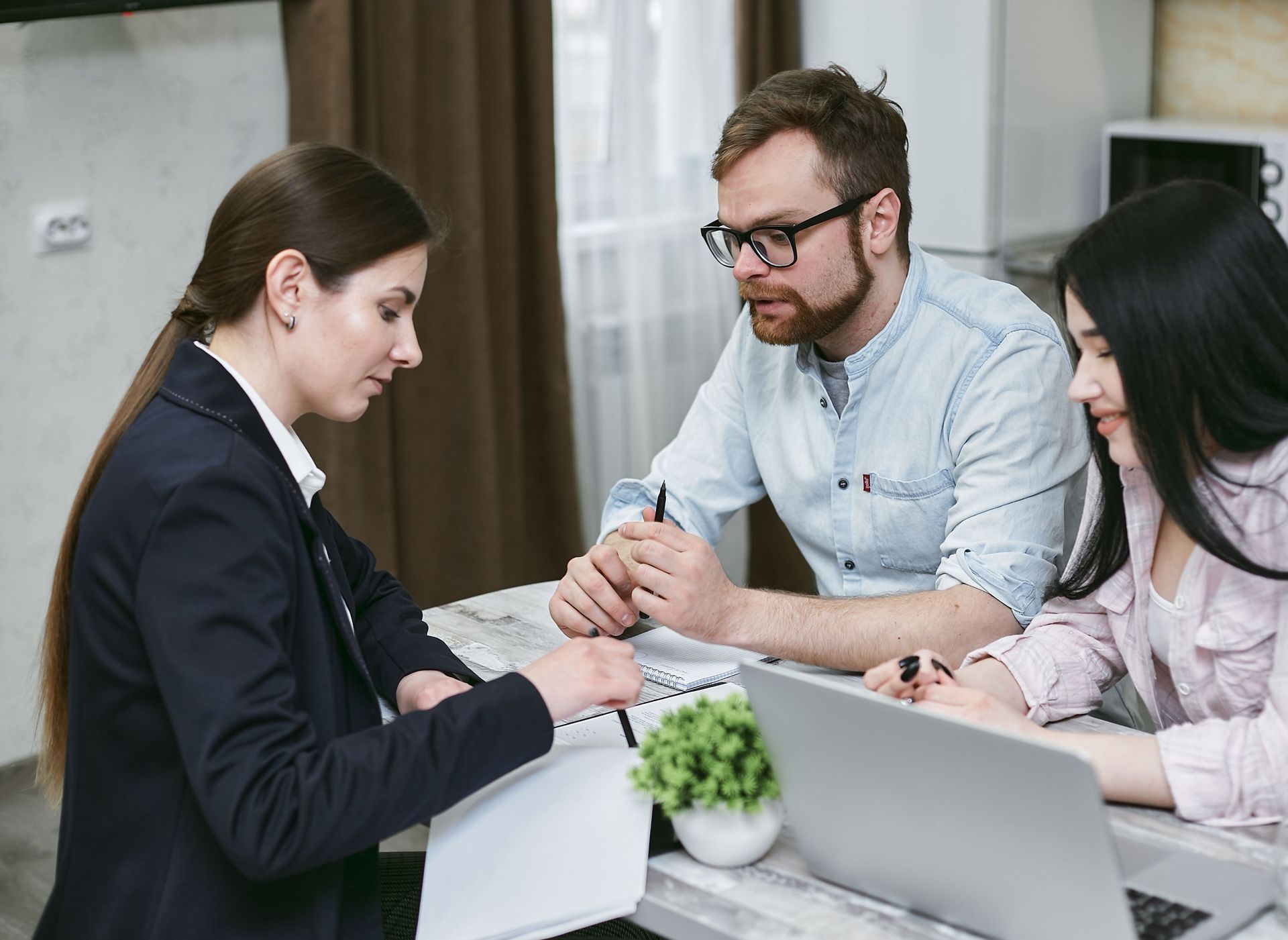 Three coworkers in a meeting, discussing life insurance documents at a laptop in a bright office.