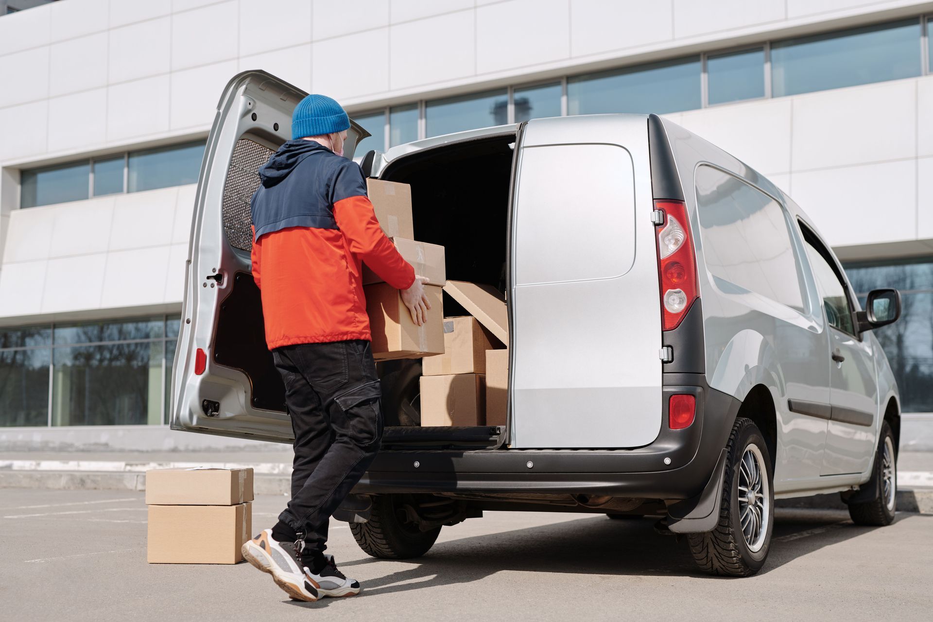 Person loading cardboard boxes into a silver van outside a building