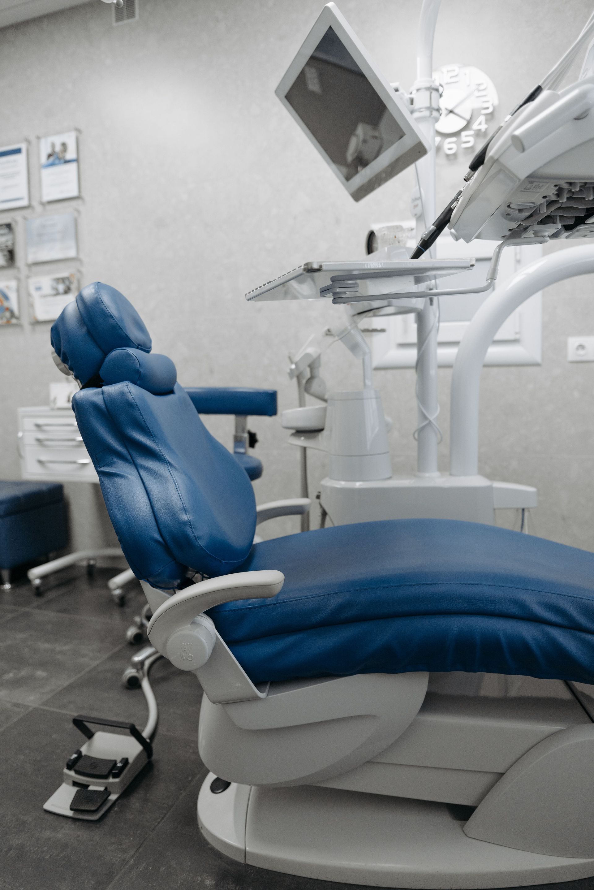 Blue dental chair in a modern exam room with overhead treatment monitor and equipment