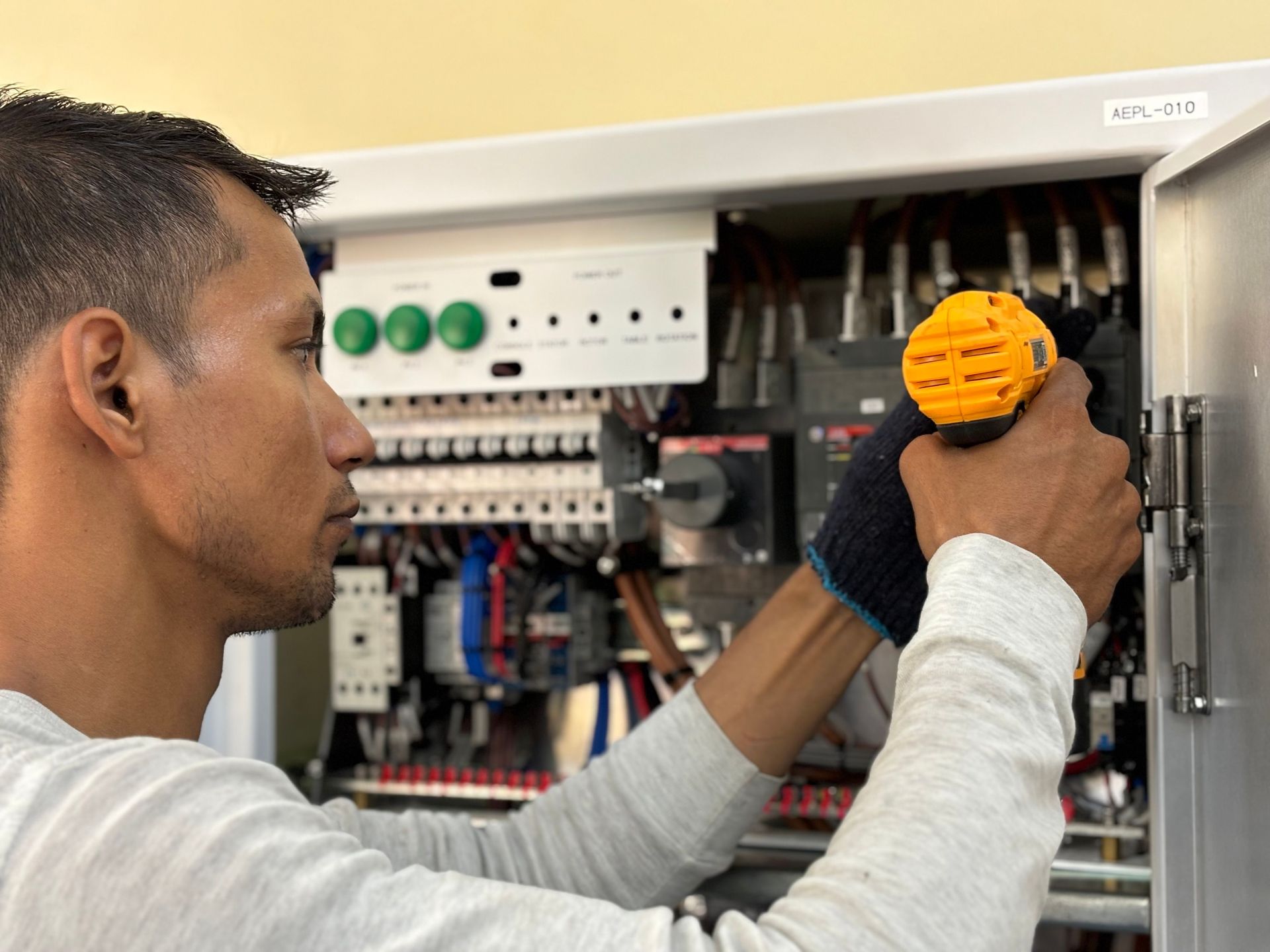 Technician tightening a screw in an open electrical panel with a yellow screwdriver
