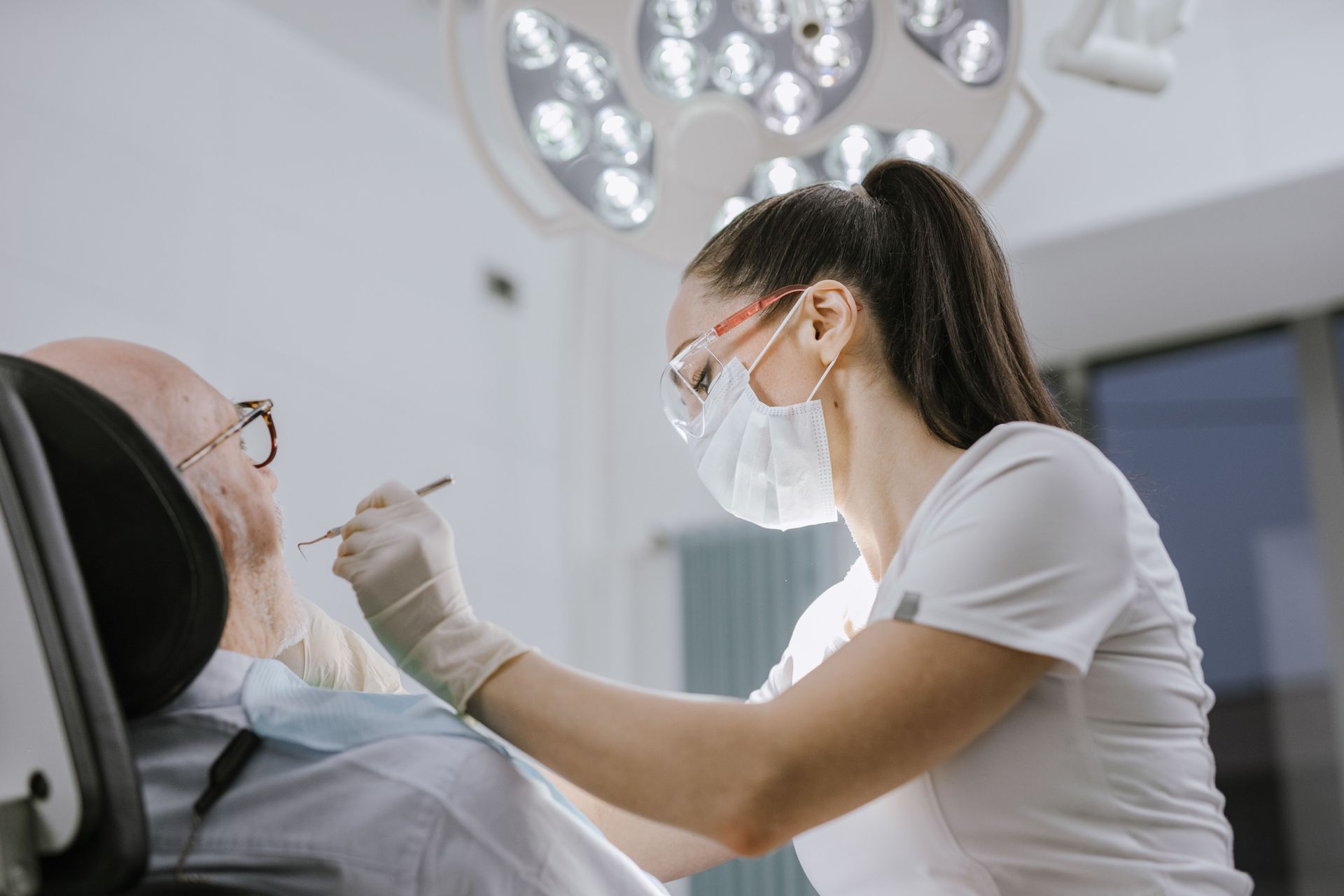 Dentist wearing a mask examines a patient in a bright dental office.