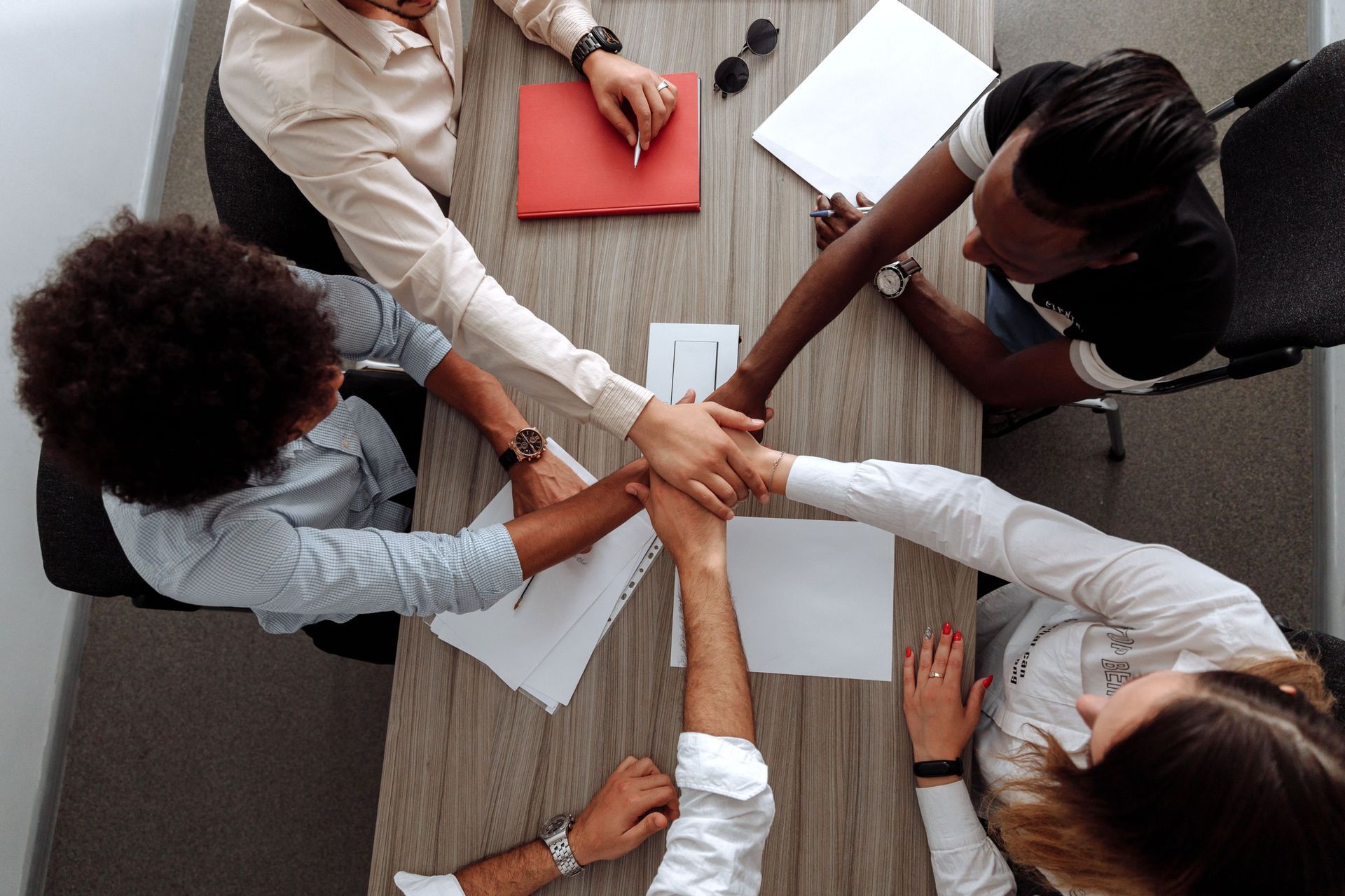 Group of coworkers stacking hands over a conference table with papers and notebooks during a meeting