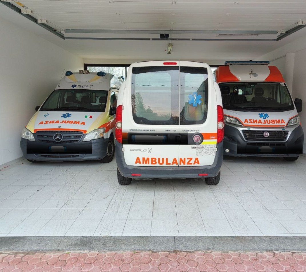 Tre ambulanze parcheggiate all'interno di un garage, con il veicolo centrale rivolto in avanti e quelli laterali angolati verso l'interno.