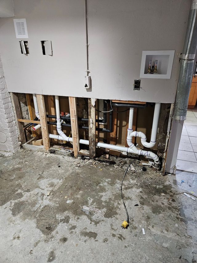 A person uses a wrench to tighten a metal pipe connector under a sink.