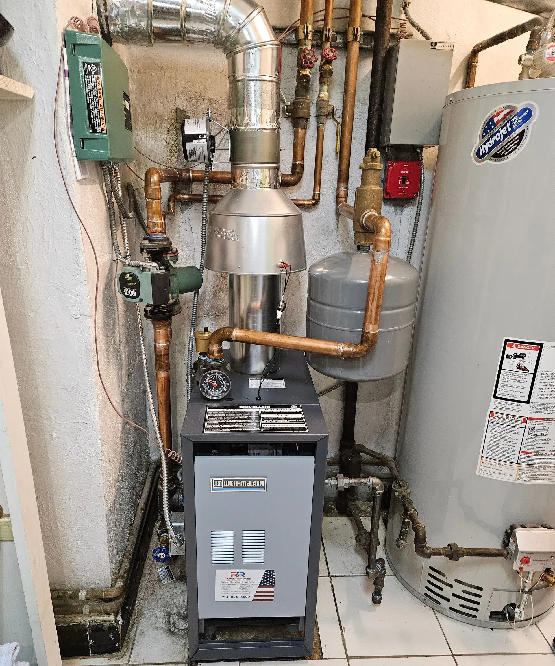 A residential boiler system with copper pipes, a gray expansion tank, and a water heater in a tiled utility room.