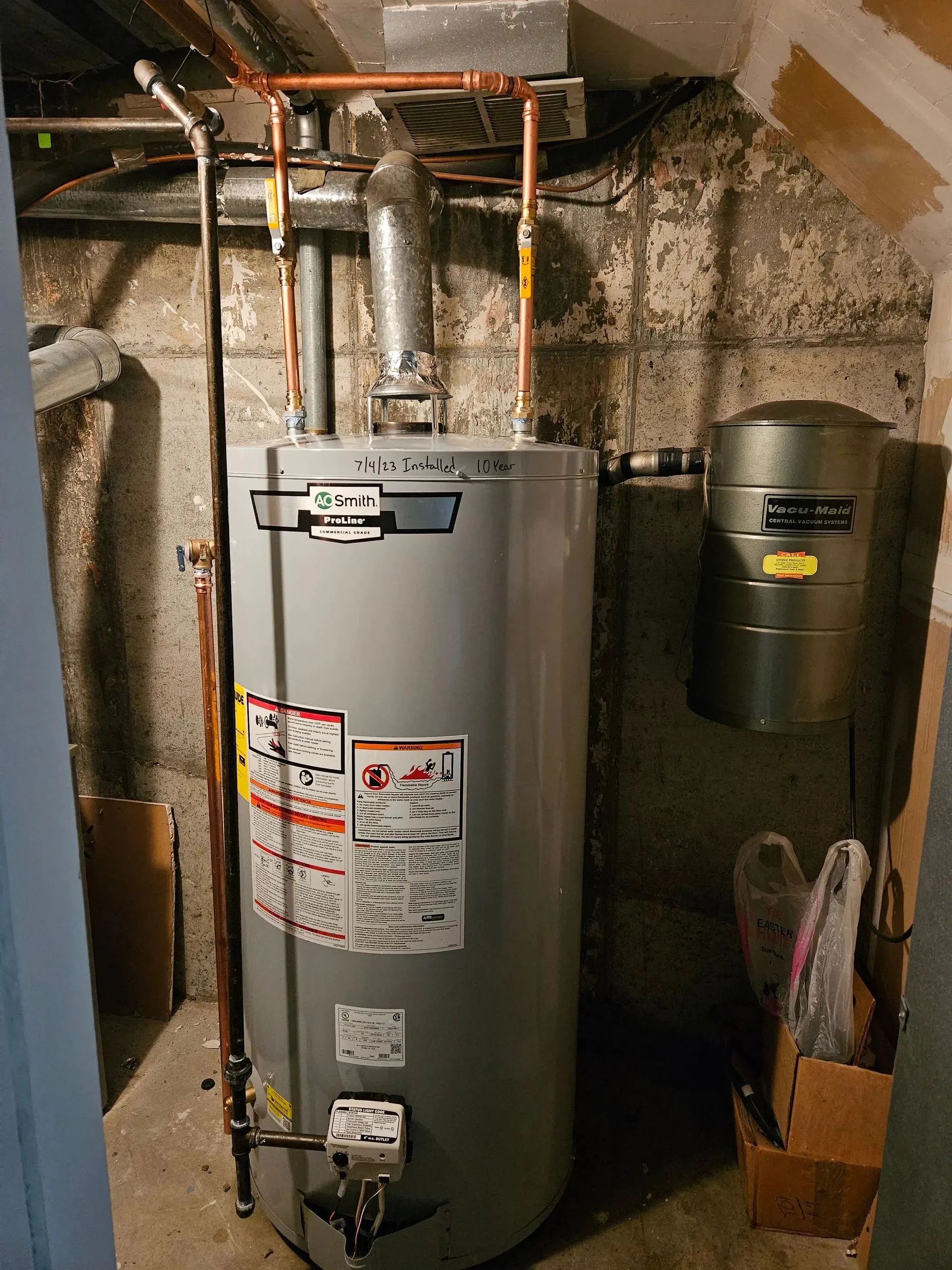 Water heater in a basement utility area with exposed pipes and a nearby expansion tank.