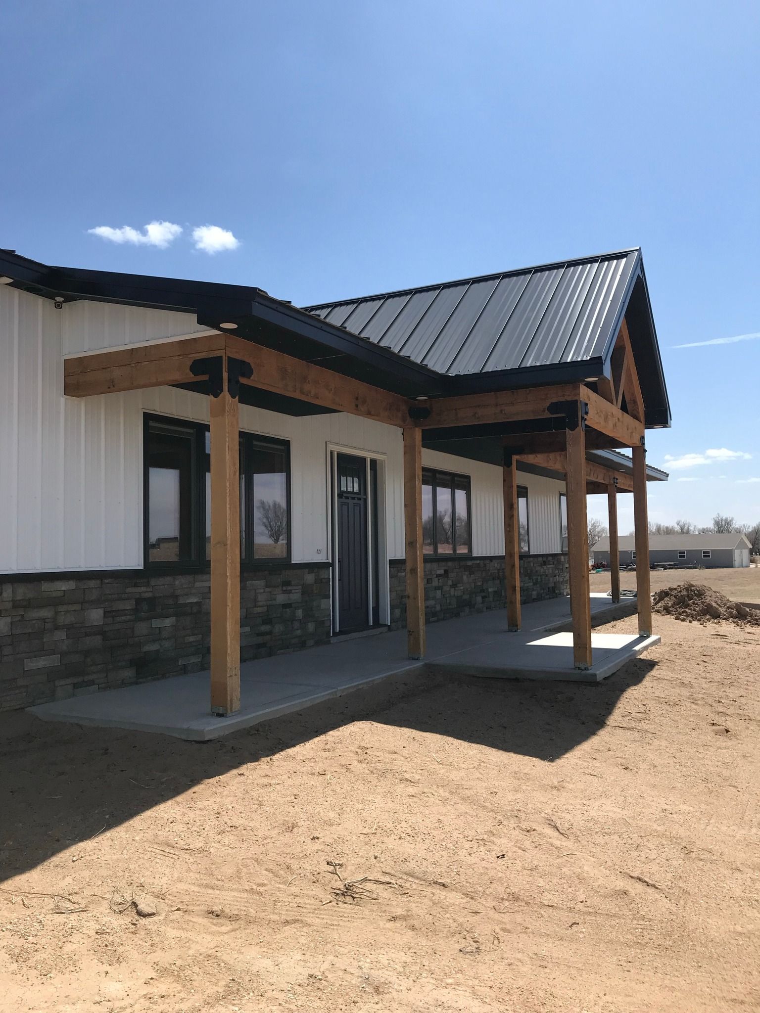 a white house with a black roof and a porch is sitting in the middle of a dirt field .