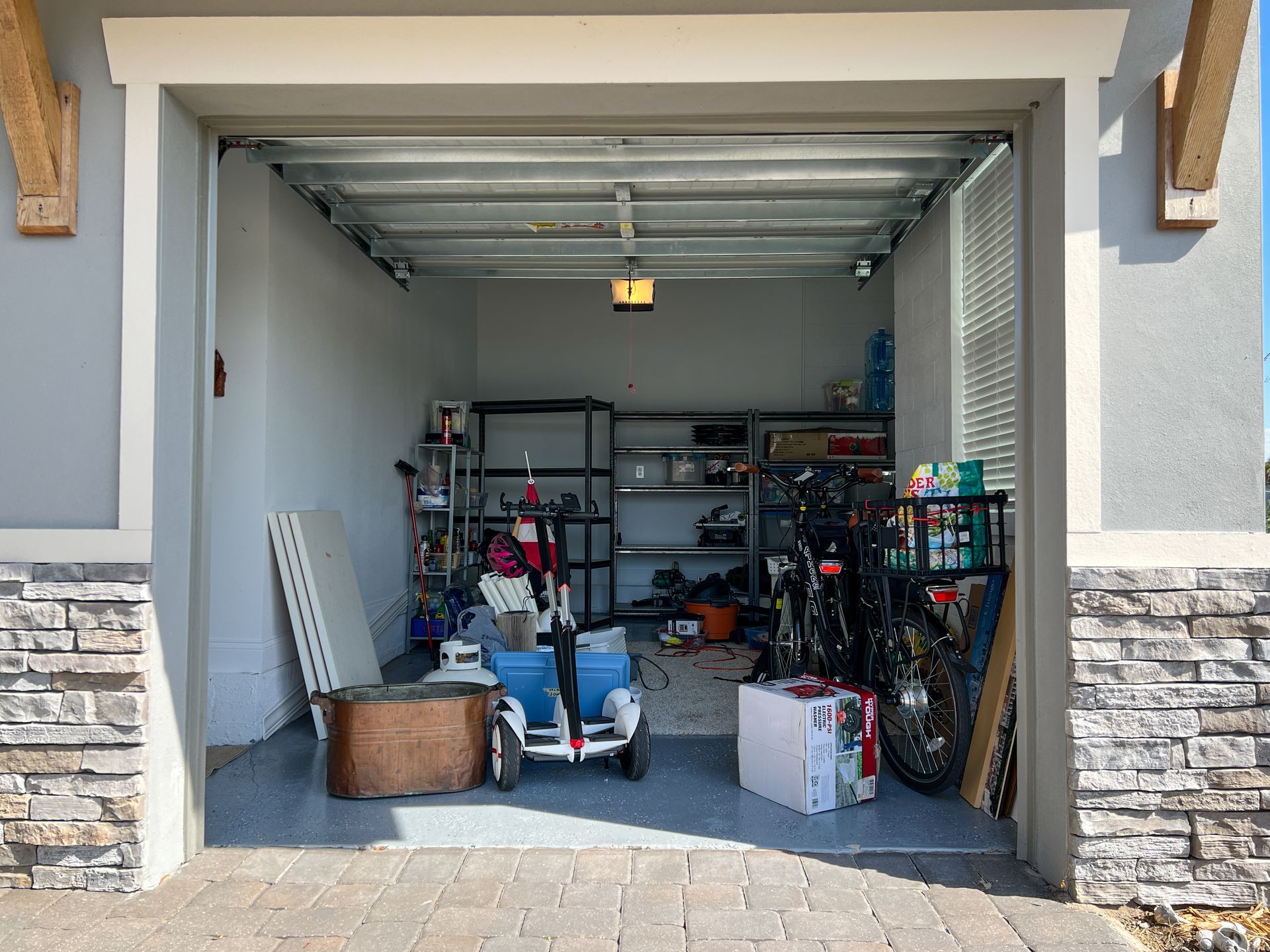 A view of a garage interior containing storage shelves, a mobility scooter, a bicycle, and various boxes.