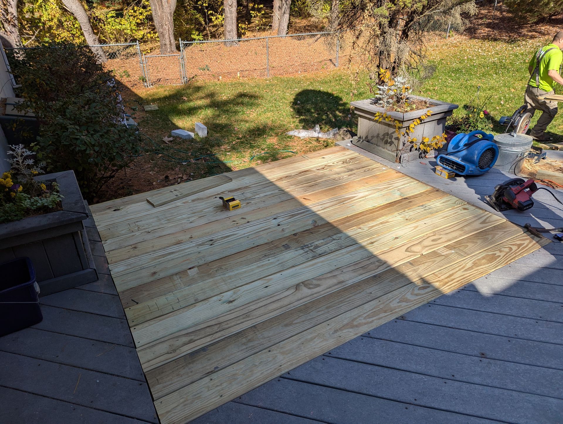 New light-colored wooden deck planks are being installed over a section of an existing dark gray deck in a backyard.