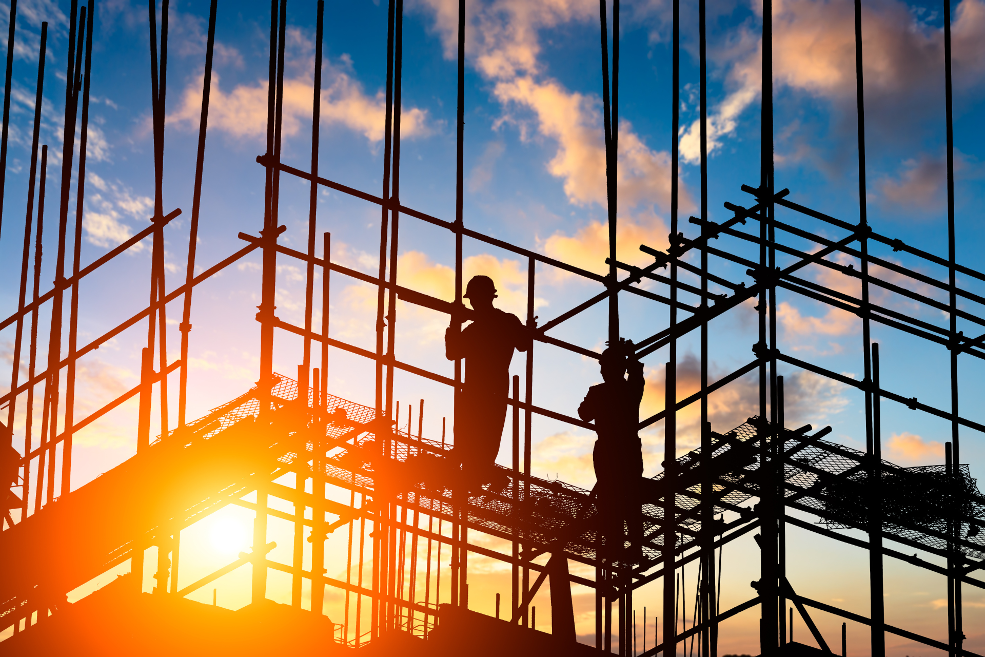 Construction workers on scaffolding at sunset.